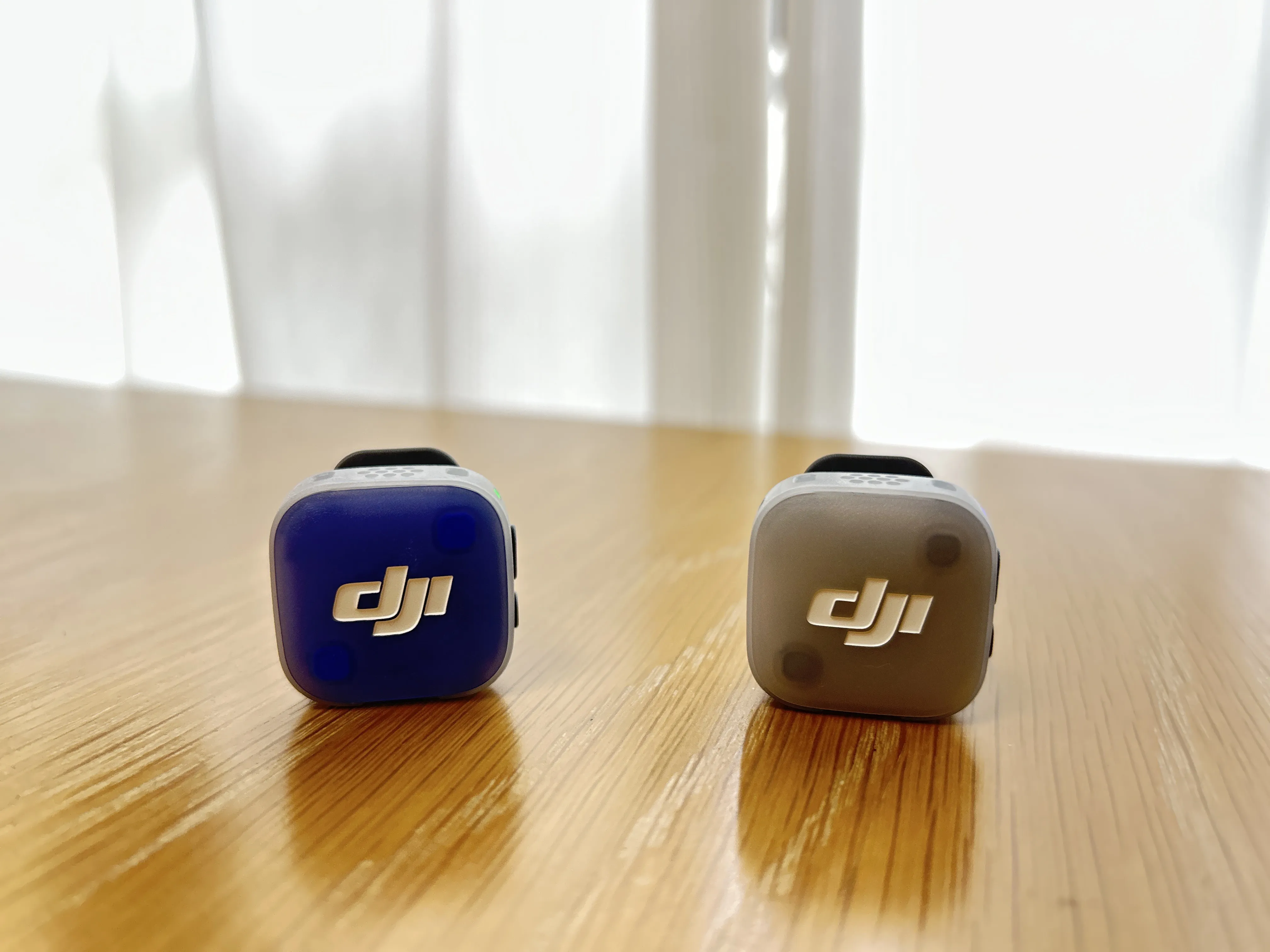 木のテーブルに置いたDJI Mic Mini 2の送信機2つ（紫とグレー）