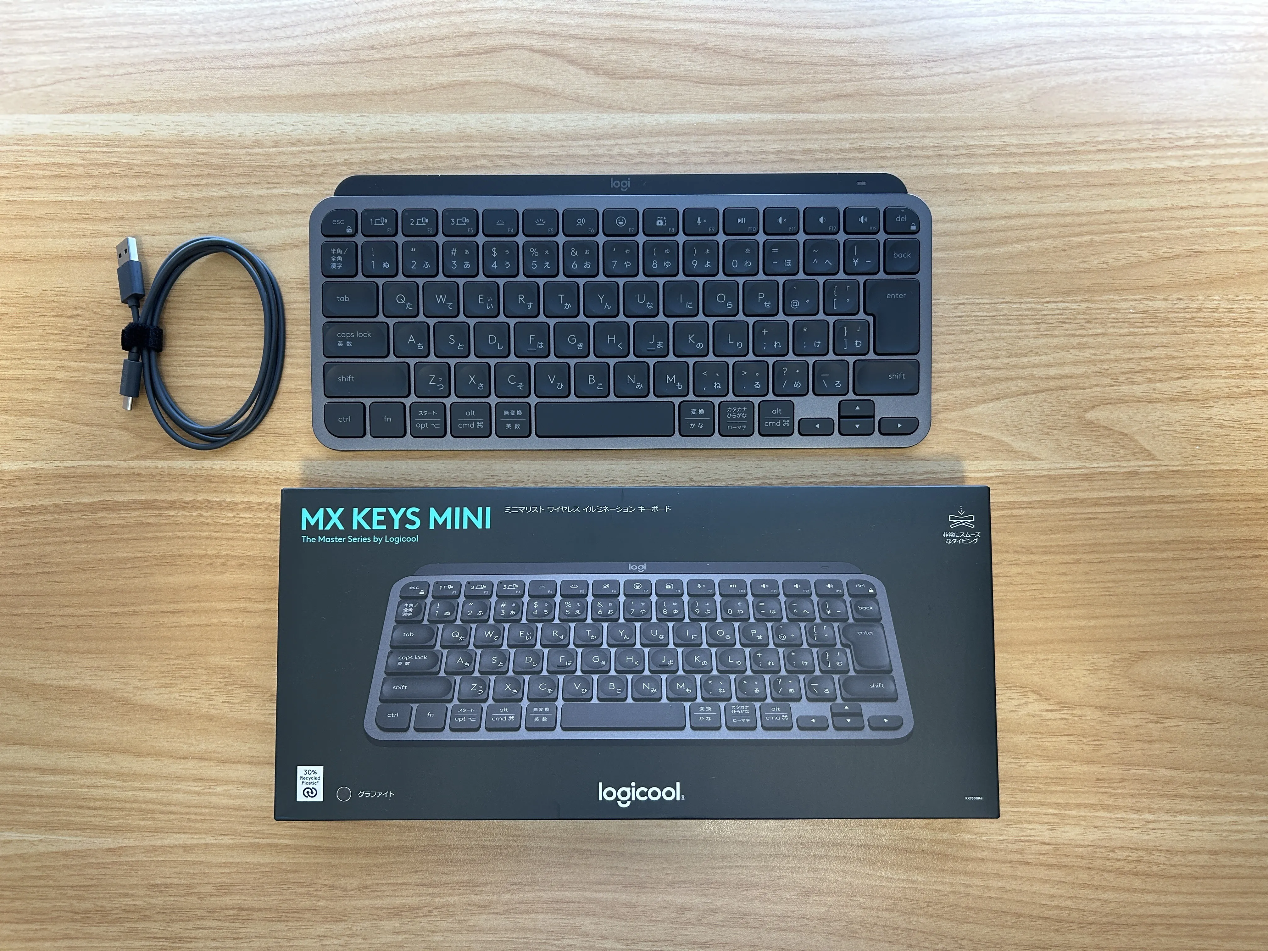 MX Keys Mini本体、付属の充電ケーブル、パッケージを木目の机に並べた写真