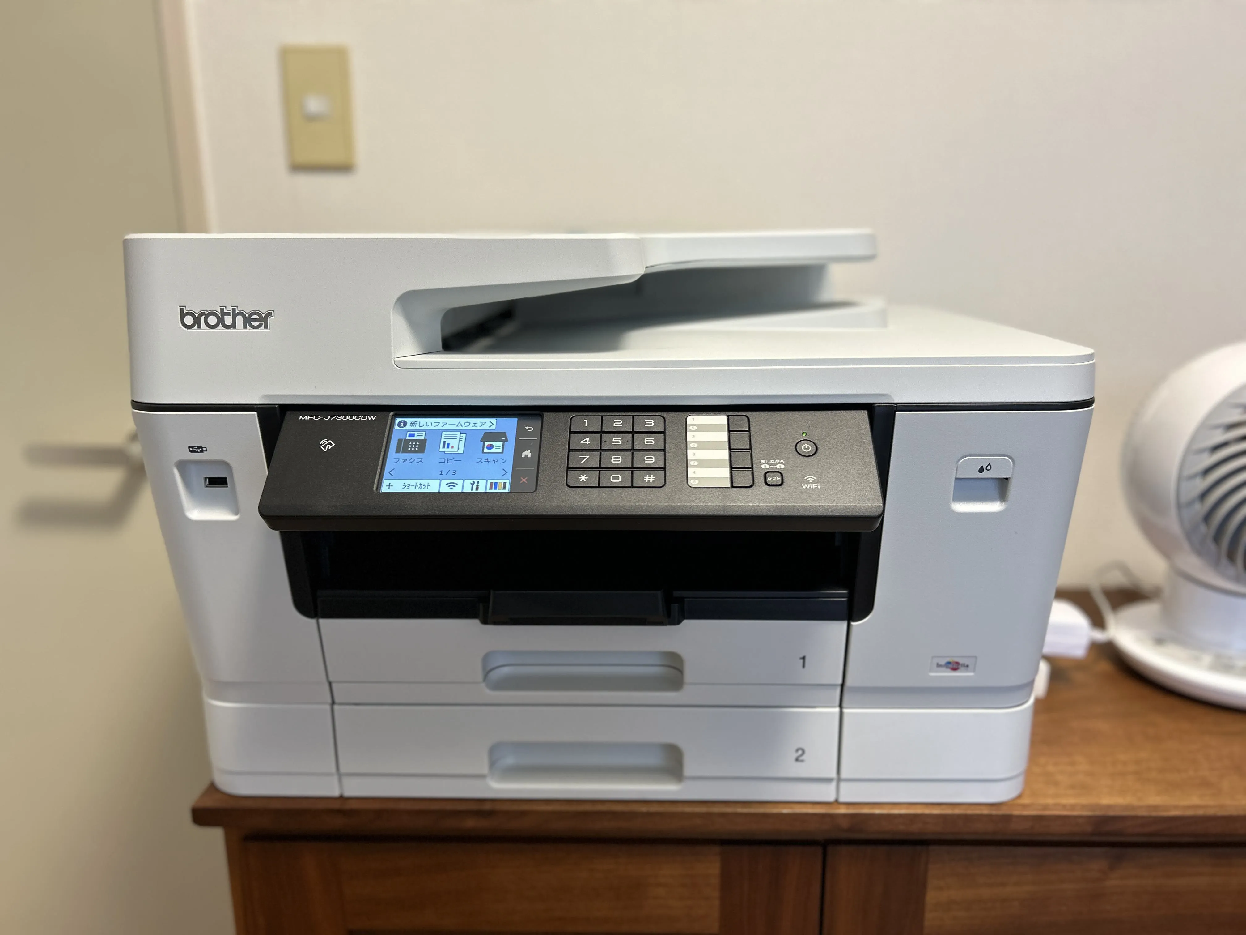 リビングの木製チェストに置いたMFC-J7300CDWの正面。2段の用紙トレイと操作パネルが見える